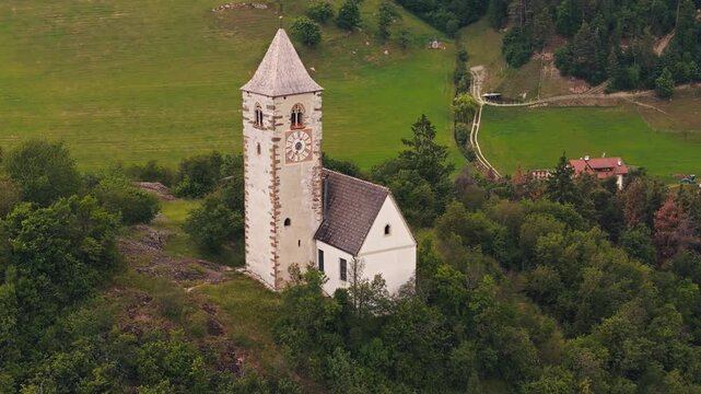 Bell tower of Chiesa di Santa Verena with pasture strips, aerial view. Alpine countryside context in northern Italy