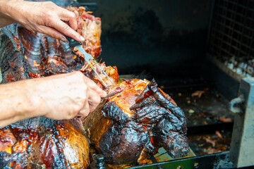 Chef Hands cutting whole grilled pork for steaks with knife. Pig grilled traditional coal and fire. The little piglet is roasted whole on an open fire. Pig on the spit