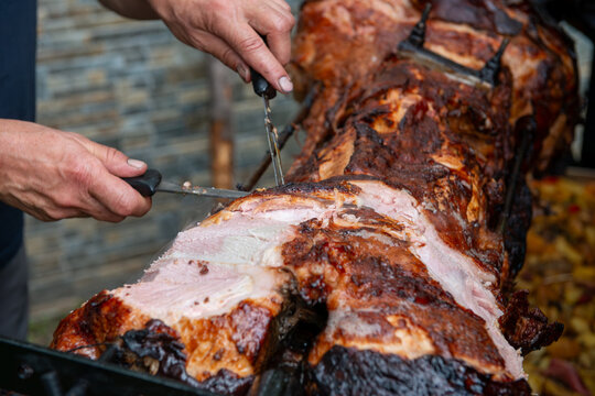 Chef Hands cutting whole grilled pork for steaks with knife. Pig grilled traditional coal and fire. The little pig is roasted whole on an open fire. Pig on the spit