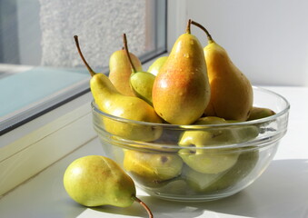 Juicy ripe sweet pears in a transparent glass bowl on a sunny windowsill.