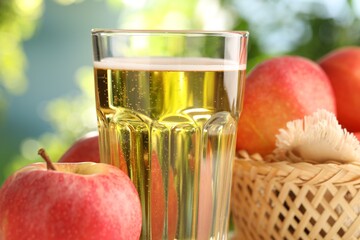 Delicious cider in glass and apples on blurred background, closeup
