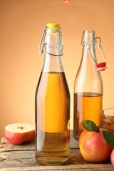Delicious cider in bottles, glass and apples on wooden table against orange gradient background, closeup