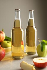 Delicious cider in glass bottles and apples on gray table against light background