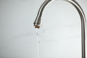 Save water concept. Stream of water flowing from tap against light background, closeup