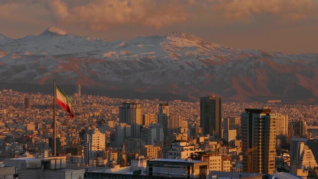 Golden sunset light over Tehran city with the Iranian flag waving in the foreground and the snow-covered Alborz mountains in the background, blending urban life with majestic nature.