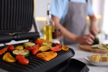 Man cutting zucchini while cooking vegetables on electric grill in kitchen, closeup