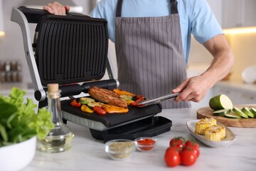 Man cooking vegetables and meat on electric grill in kitchen, closeup