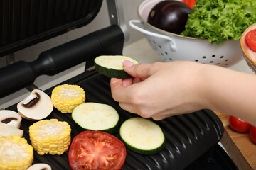 Woman putting zucchini onto electric grill at table, closeup