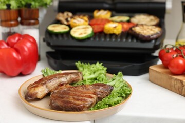 Electric grill with vegetables and tasty meat on white table, selective focus