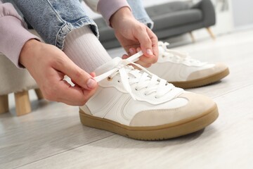 Woman tying shoelace of white sneaker indoors, closeup