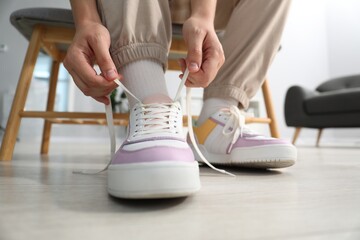 Woman tying shoelace of colorful sneaker indoors, closeup