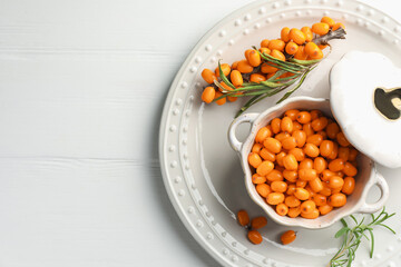 Fresh sea buckthorn berries in dish and leaves on wooden table, top view. Space for text