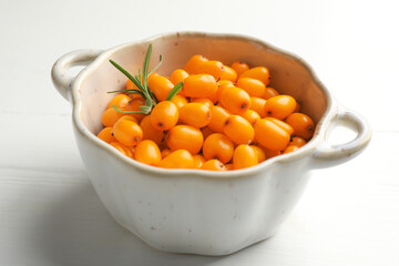 Fresh sea buckthorn berries in dish and leaves on white wooden table, closeup