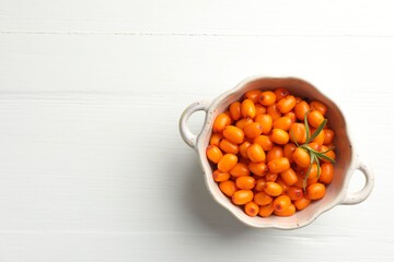 Fresh sea buckthorn berries in dish and leaves on white wooden table, top view. Space for text