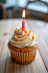 Delicious birthday cupcake with a single burning candle sits on a light wood table, celebration, cupcake