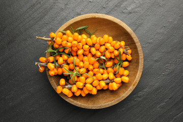 Fresh sea buckthorn berries with leaves in bowl on black table, top view
