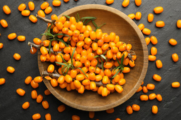 Fresh sea buckthorn berries with leaves in bowl on black table, flat lay