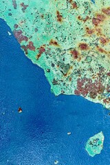 Close-up of old peeling green paint with patches of blue and rust on corroded metal surface, perfect for backgrounds and grunge design.