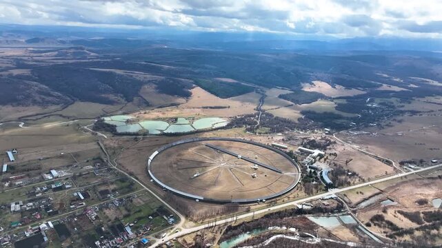 Karachay Cherkessia, Russia - September 12, 2024: A high, sweeping aerial panorama of the massive circular RATAN 600 radio telescope, surrounded by the Zelenchukskaya settlement, artificial ponds, rol