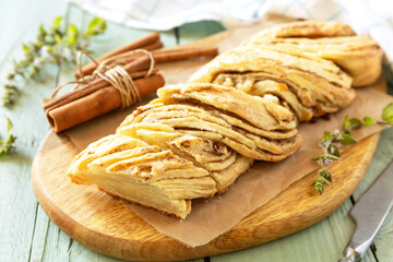 Braided cinnamon sweet bread on rustic wooden board with cinnamon sticks and herbs.
