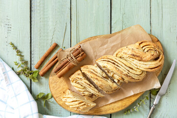 Braided cinnamon sweet bread on rustic wooden board with cinnamon sticks and herbs.