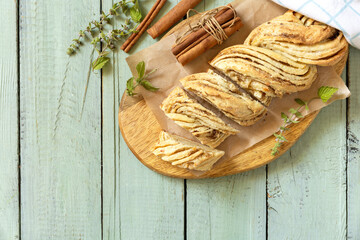 Braided cinnamon sweet bread on rustic wooden board with cinnamon sticks and herbs. Top view flat lay background. Copy space.