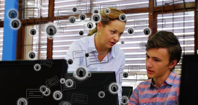 Teacher walking to student workstation in computer lab, tapping smartphone and guiding coding task - Powered by Adobe