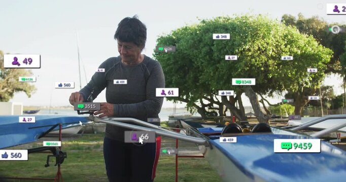 Senior woman picking up spanner and tightening blue rowing shell oarlock for alignment in boatyard