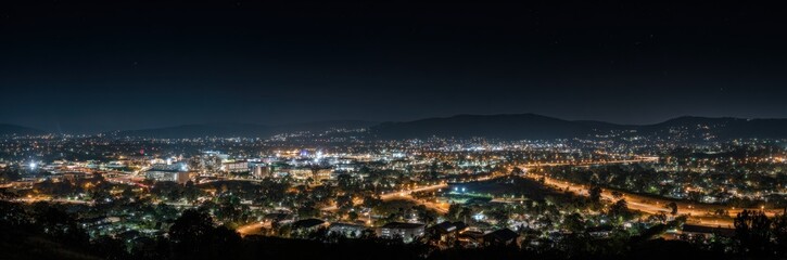 A sprawling cityscape glows brightly at night, nestled in a valley and framed by dark mountains.