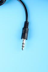 A close-up of a stereo jack on a black wire against a blue background.