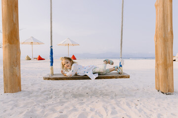 Happy girl plays on swings on tropical beach, enjoy childhood