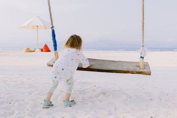 Little girl playing with swings on tropical beach, enjoy childhood