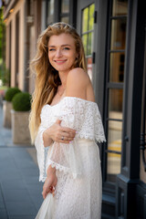 Woman in white lace dress smiles warmly outside a charming building