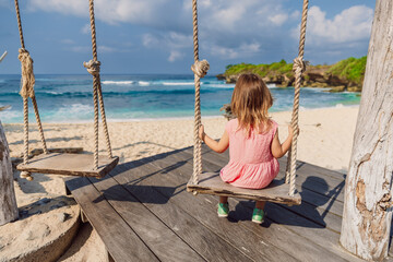 Child girl on swings at tropical beach with blue sea, enjoy childhood