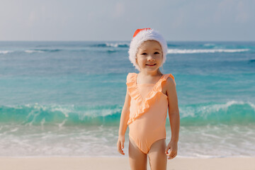 Little girl in ocean beach with Christmas hat. Portrait of happy smiling girl