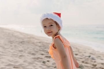 Little girl in ocean beach with Christmas hat. Happy smiling girl
