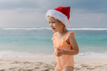 Little child girl in tropical beach with Christmas hat.