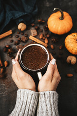 Female hands holding mug of hot chocolate, pumpkins and spices on rustic background, cozy autumn scene
