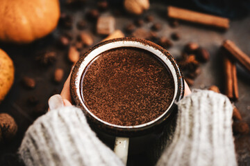Female hands holding mug of hot chocolate, pumpkins and spices on rustic background, cozy autumn scene