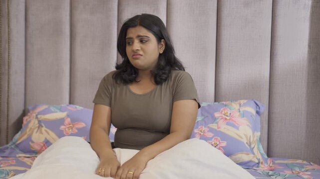 Pregnant Indian lady sitting on a bed - Expecting lad feeling uncomfortable  stressful period  hormonal change . A pregnant woman going through stressful time - mood swings  frustration  irritation...