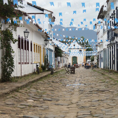 Rua de cidade hist&oacute;rica brasileira decorada com bandeirinhas azuis, destacando arquitetura colonial e atmosfera festiva.