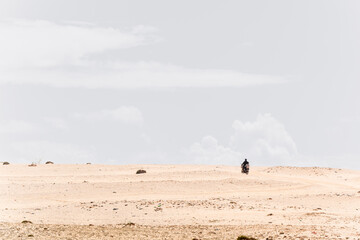 Two occupants of a motorcycle ride through the Moroccan desert on a sunny morning with blue sky and clouds. Copy Space
