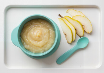Baby food mashed pear in bowl with fresh pear slices