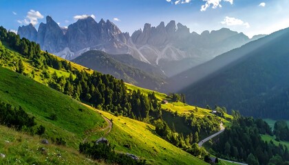 Obraz premium Sunlit mountain valley with rolling green hills, a winding road, and a distant, dramatic mountain range
