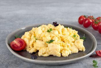 Scrambled eggs with green onions and tomato on a gray plate on gray background. Healthy breakfast. 