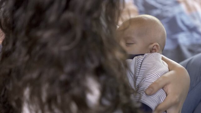 A tired Indian mother holding her adorable son in her arms while he is sleeping - breast feeding a baby. Young housewife and her little baby resting together on the bed - happy childhood  good drea...