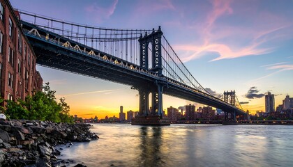 Obraz premium Sunset view of a large suspension bridge over a river, with city skyline in the background