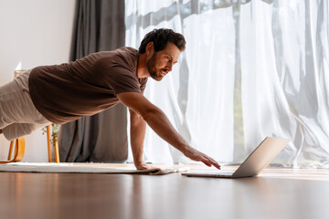 Fototapeta premium Handsome, middle aged man training at home with online fitness workout guidance
