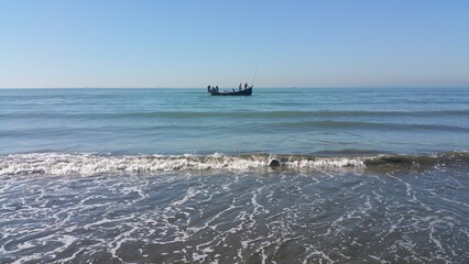 Fishing boat sailing on the calm blue ocean, gentle waves lapping at the shore on a clear sunny day, capturing a peaceful maritime scene