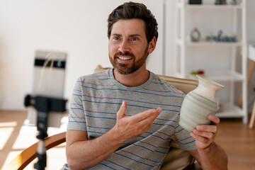 Smiling bearded man presenting handmade ceramic vase during online video lesson